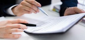 Hands holding pens pointing at document