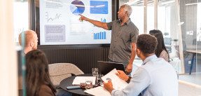 Man giving presentation to colleagues pointing to screen