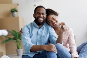 Smiling couple with keys in living room with moving boxes