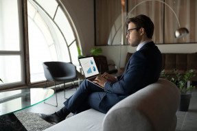 Thoughtful 30s businessman reading research report on sofa