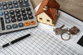 Toy house, calculator, keys, and pen on financial papers