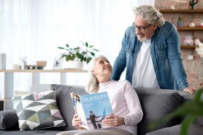 Woman on couch holding a magazine talking to a man standing behind the couch