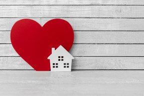 White wooden toy house against large red heart and white boards
