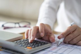 Woman in white shirt using a calculator and holding a pen to a spreadsheet