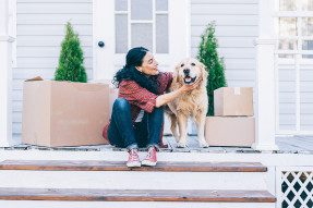 Woman on porch steps of home with a dog and moving boxes