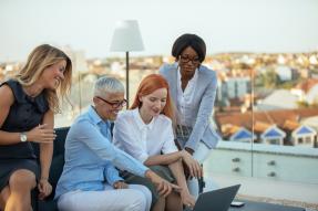 four women professionals looking at laptop
