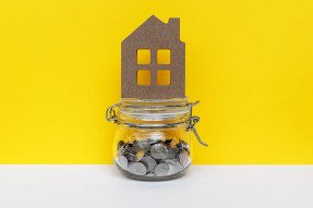 Wooden house cutout on top of a jar of money