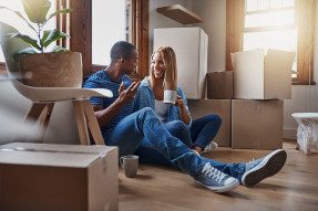 Young black couple sitting on floor of living room with moving boxes