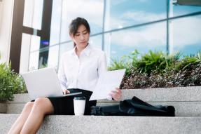 Young professional woman seated on steps with laptop and coffee 