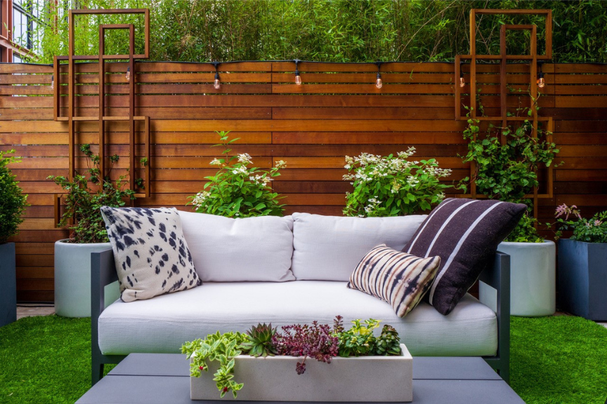 Photo of a cream colored outdoor loveseat with a darkwood fence as a backdrop