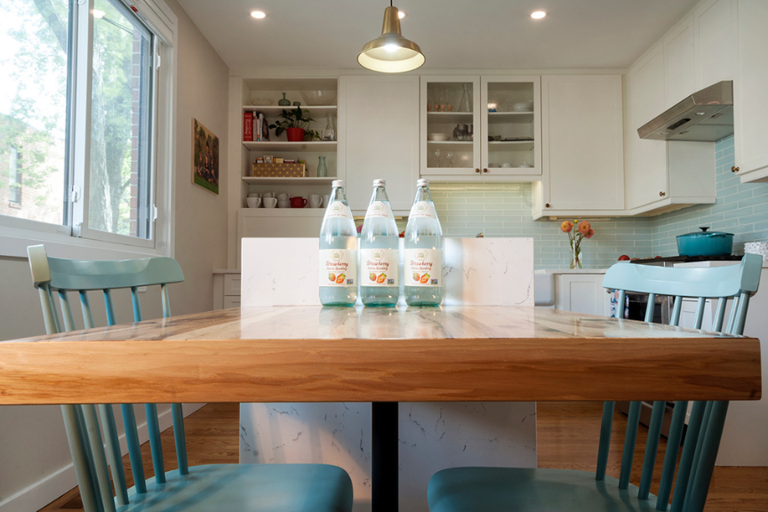 Photo of a dining room, zoomed in on the dining table, which is a light-colored wood and has 3 bottles of water on top