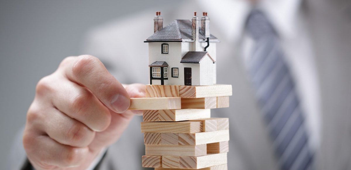 Businessman pulling Jenga puzzle pieces from underneath house model
