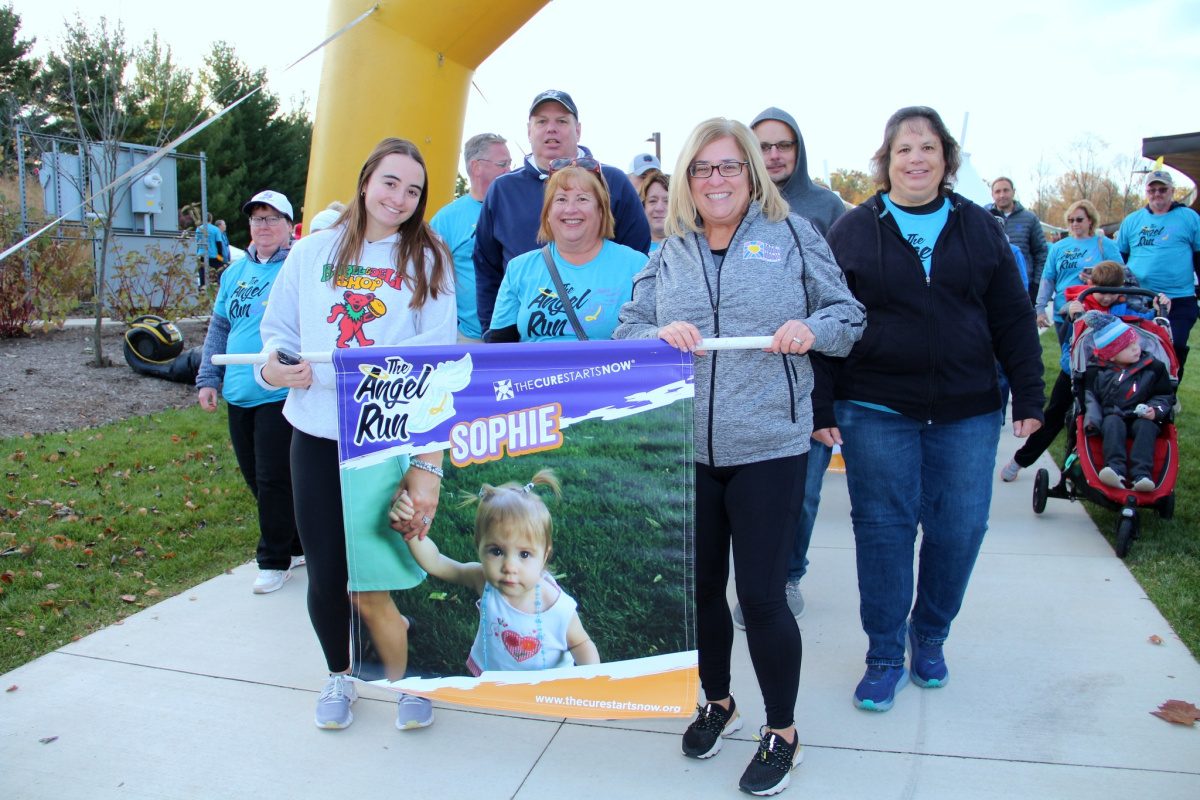 A small banner showing a picture of Sophie is held up by surrounding family and friends.