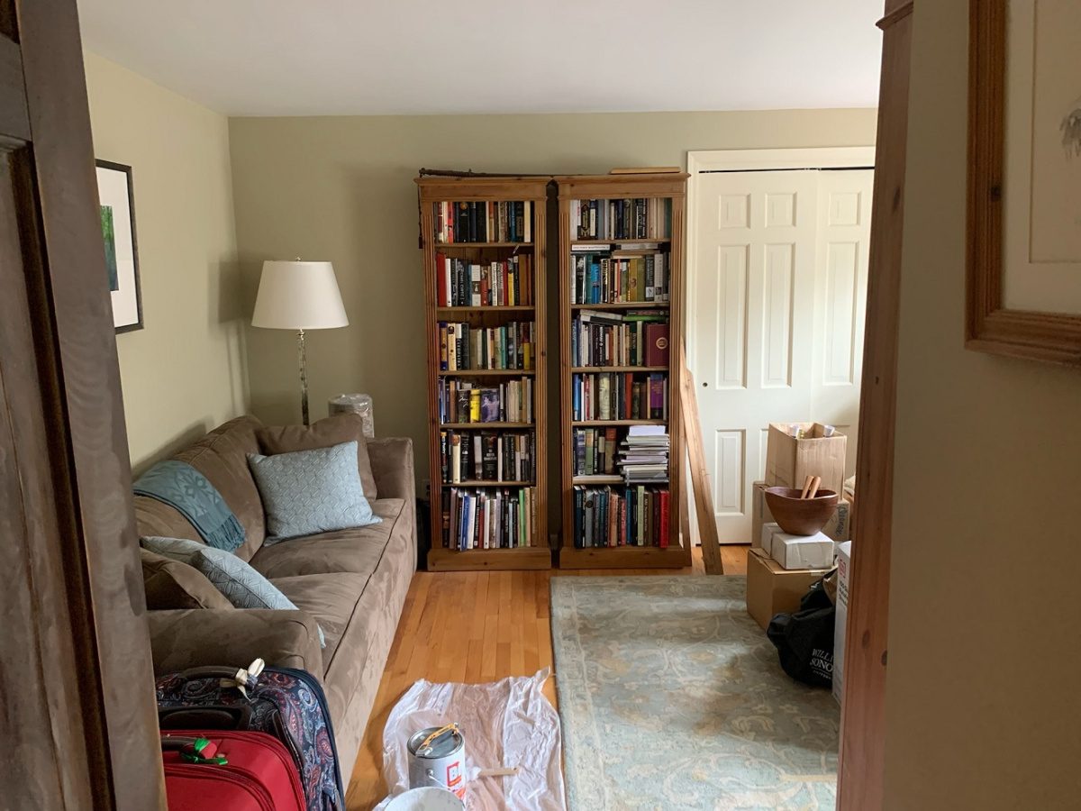 A room full of clutter (full bookshelves, oversized couch, overflow storage) before being redesigned and staged