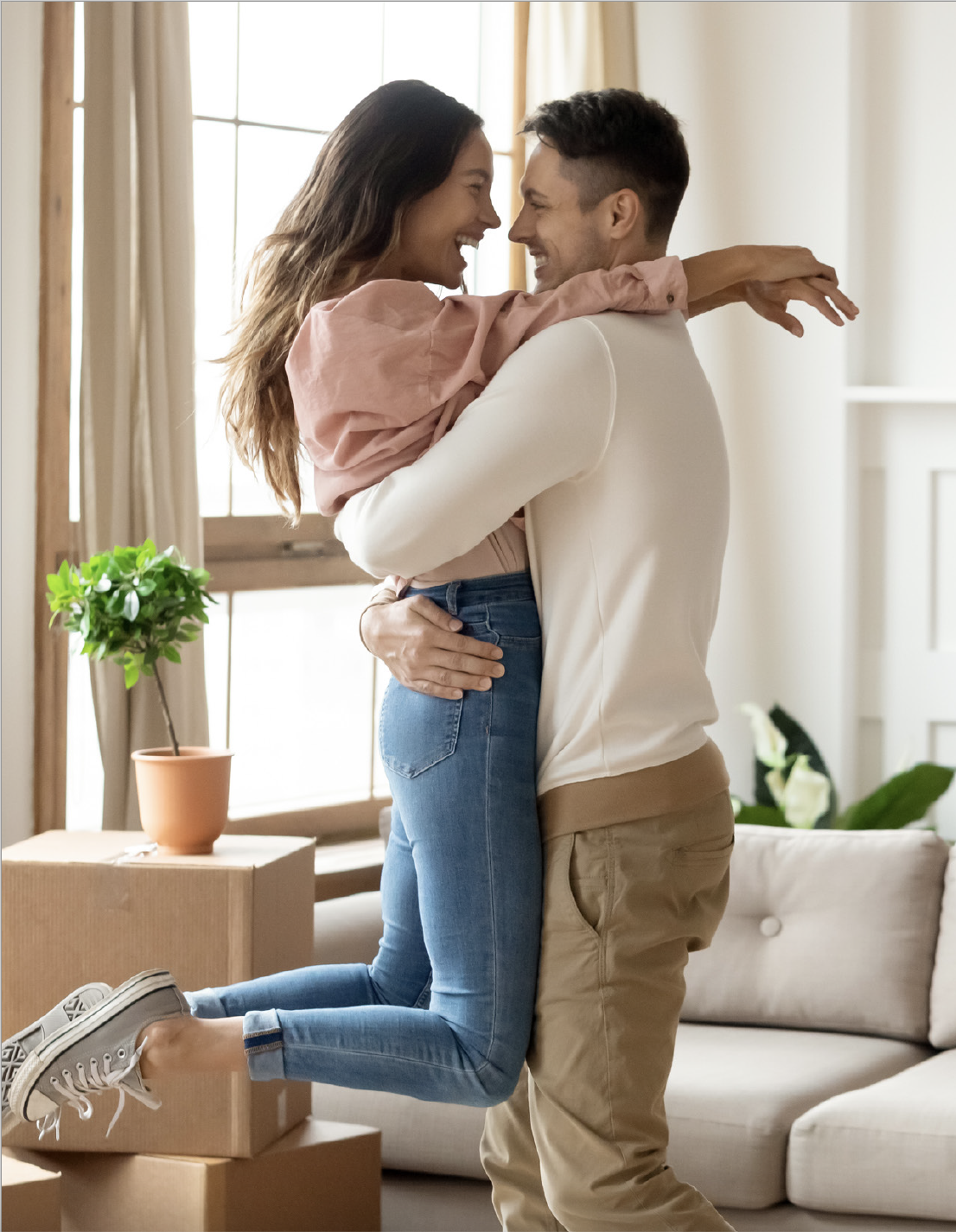 Young couple in living room with moving boxes and couch in the background