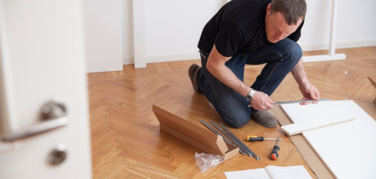 Man kneeling on floor in black shirt and jeans while assembling furniture