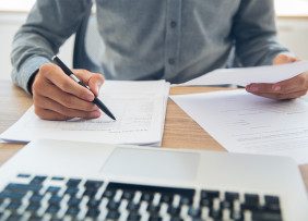 Person in front of a laptop holding a pen and reviewing papers