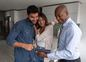 Real estate agent and clients standing in kitchen looking at tablet