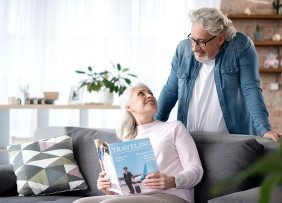 Woman on couch holding a magazine talking to a man standing behind the couch