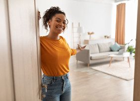 Woman at the door to her home gesturing to the living room