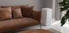 A tall, white air purifier next to a modern brown leather couch in a minimalist living room