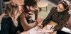 Three people sit at a table going over financial documents together.